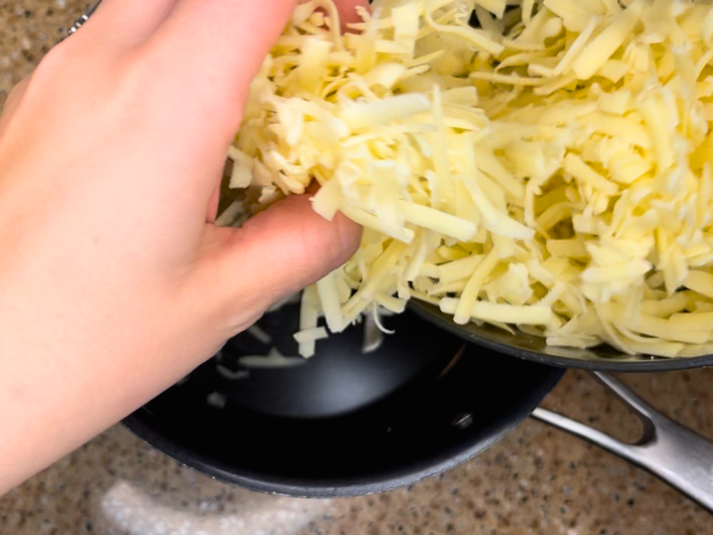 Shredded Swiss cheese being placed in a sauce pot to melt.