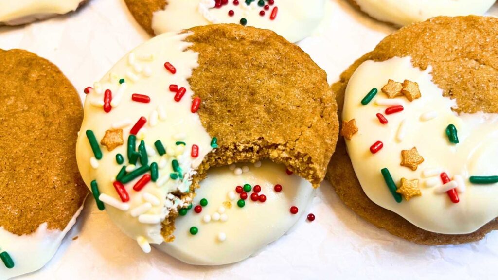 Gingerbread cookies dipped in white chocolate and decorated with festive sprinkles. One has a bite out of it.