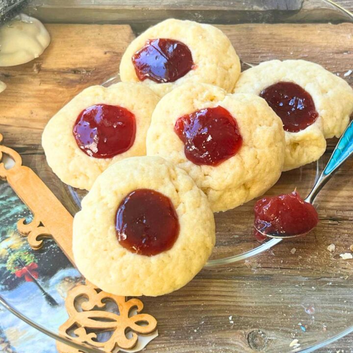 A glass plate with 5 thumbprint cookies with jam in the middle.