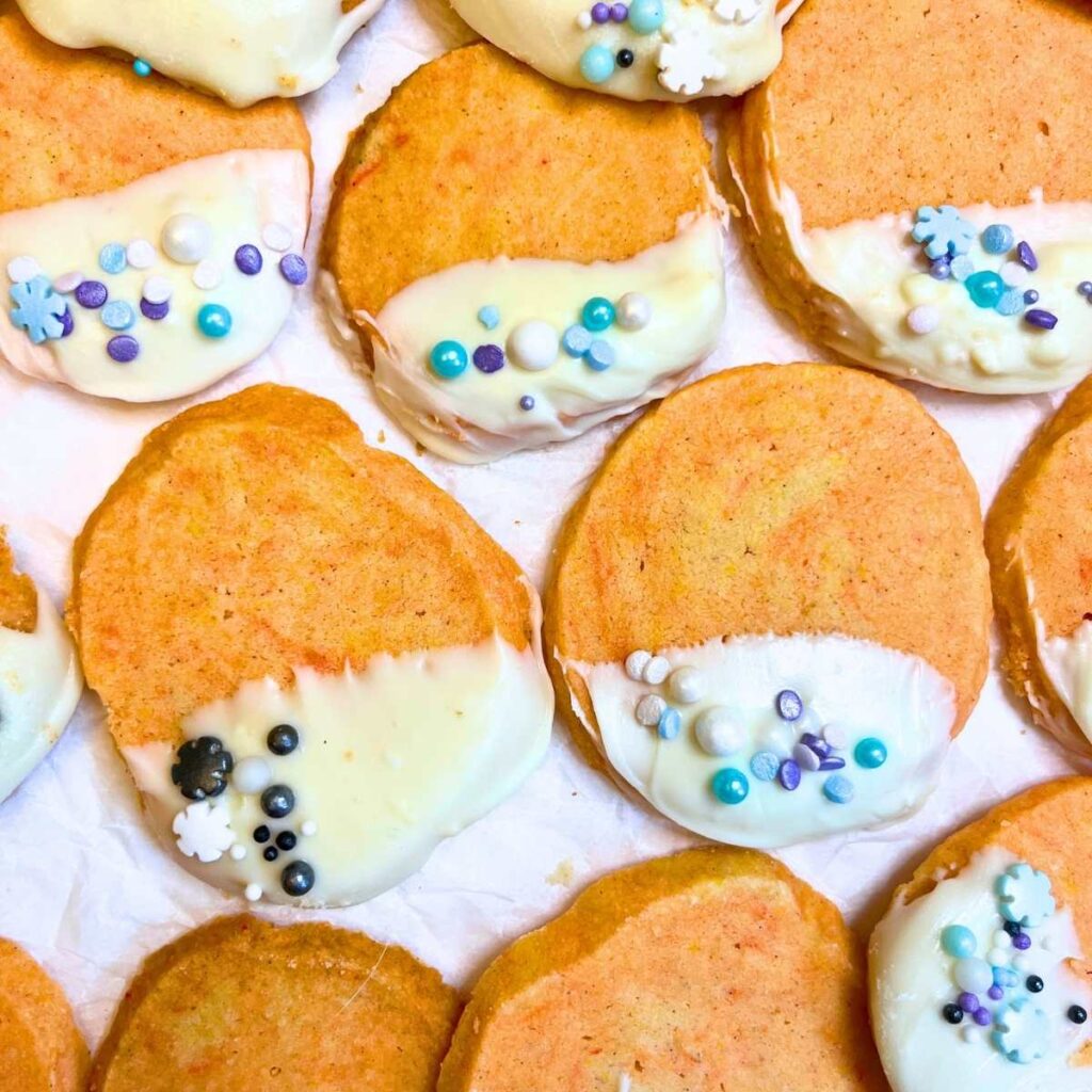 Orange shortbread cookies that are dipped in white chocolate and decorated with sprinkles