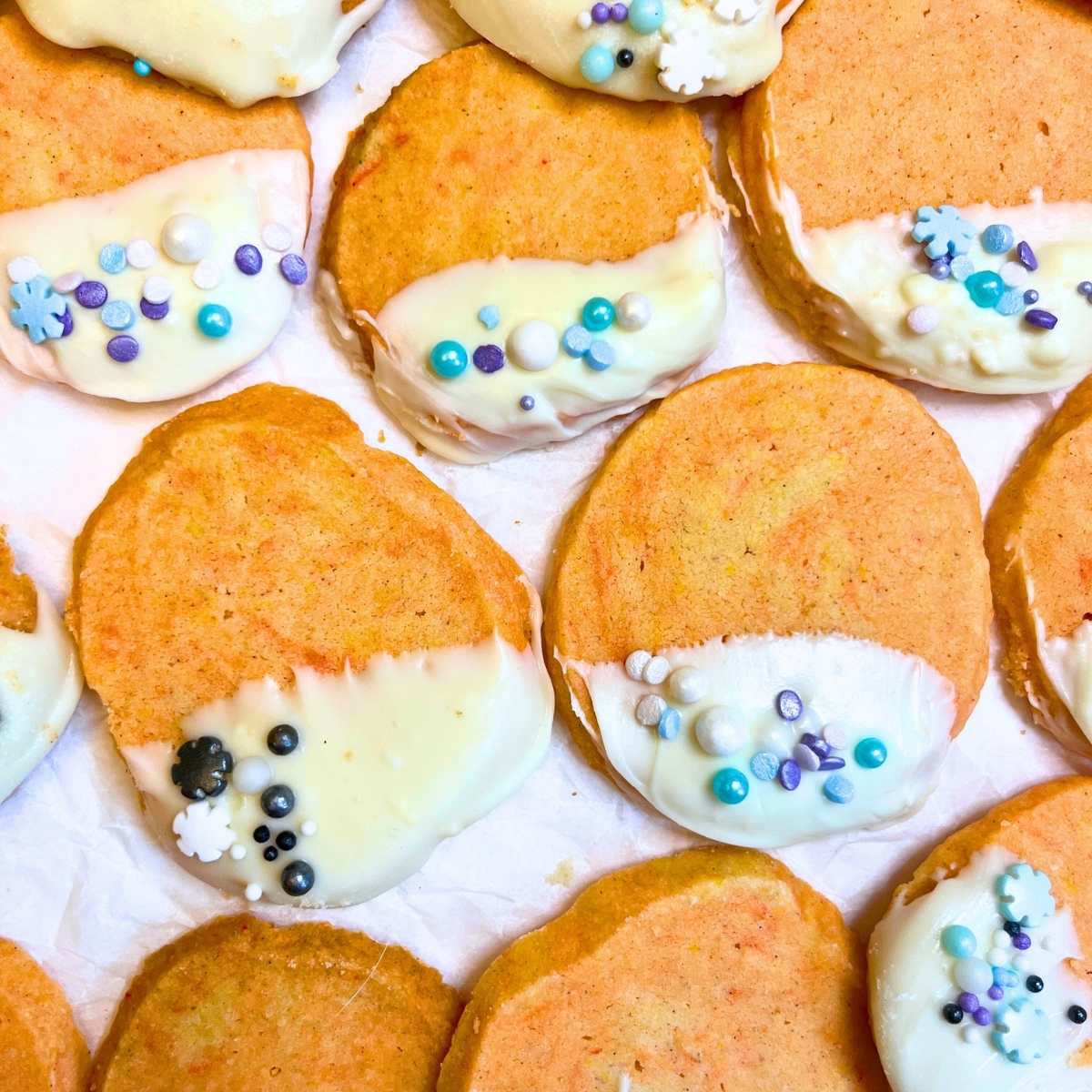 Orange shortbread cookies that are dipped in white chocolate and decorated with sprinkles