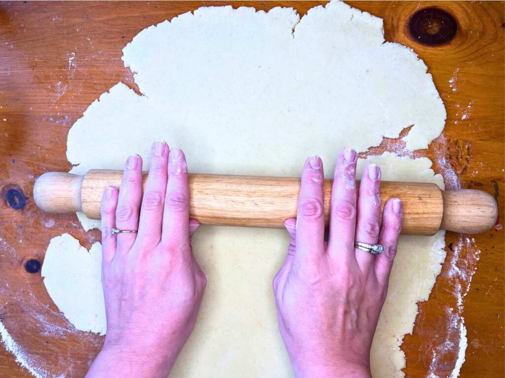 A woman rolling out sugar cookie dough with a rolling pin.