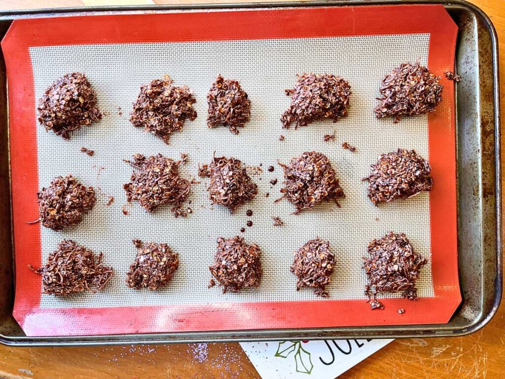 A group of chocolate haystack cookies on a lined cookie sheet.