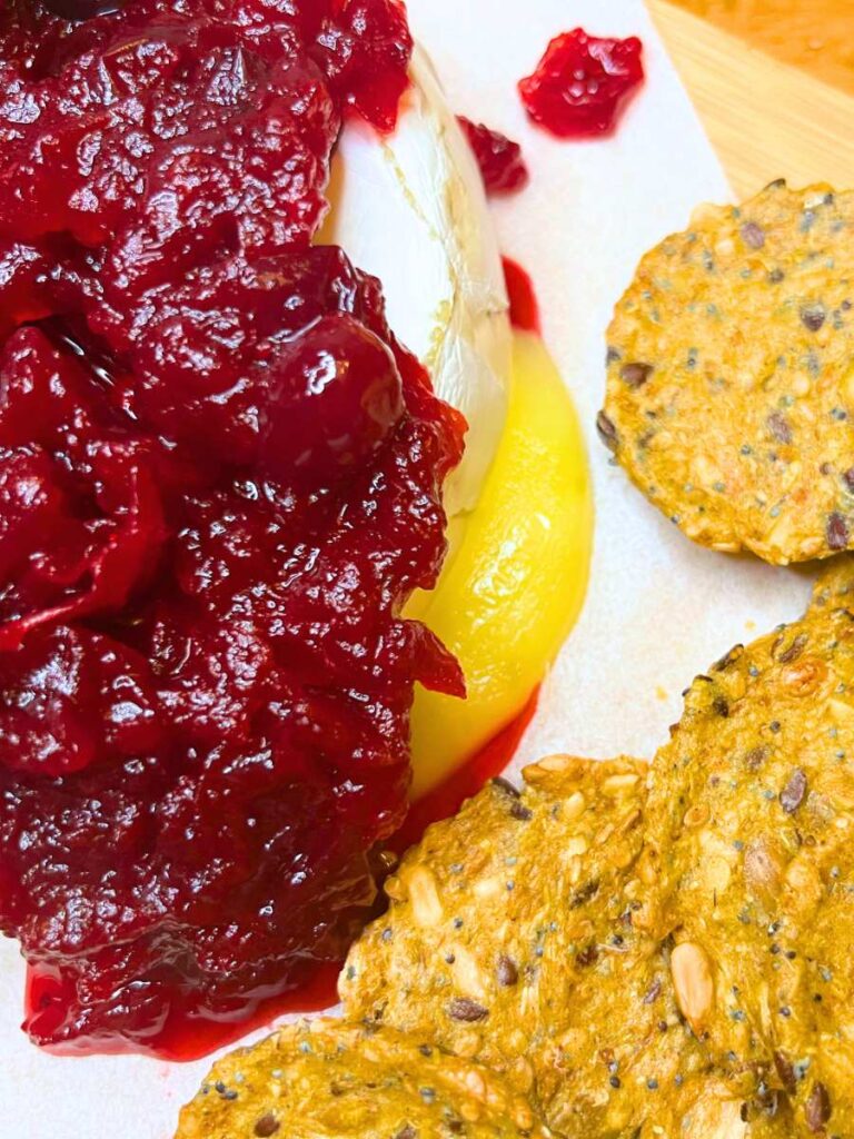 A close up look at a baked Brie with cranberry sauce on top. There are crackers to the side.