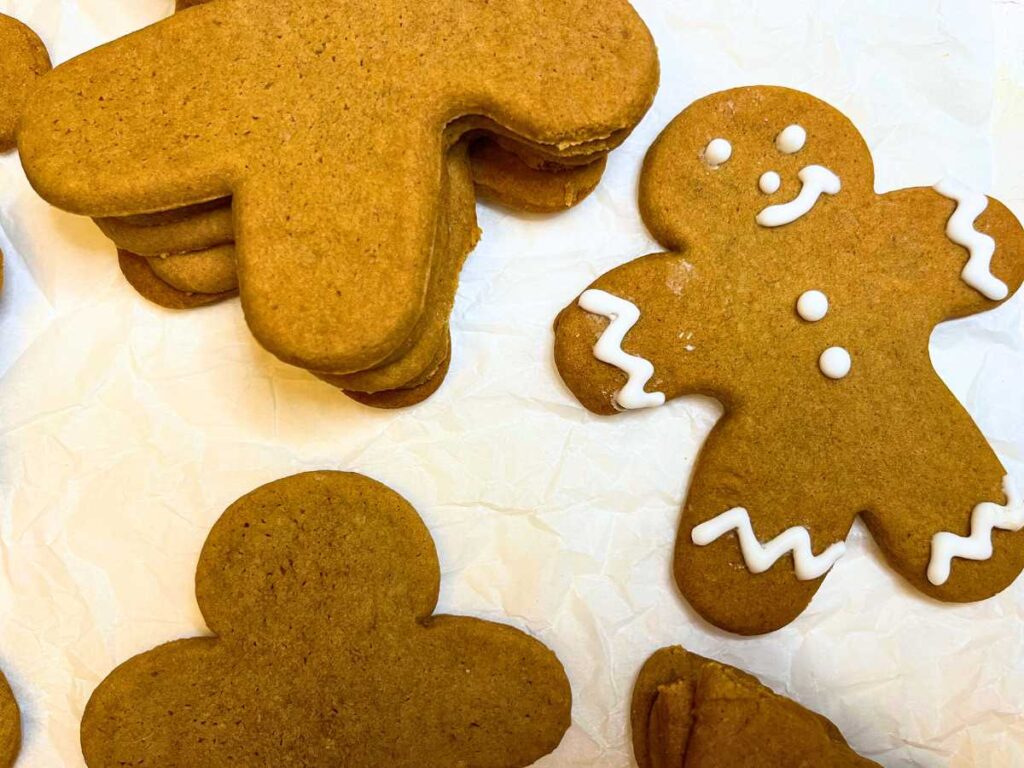 Baked gingerbread men on a piece of parchment paper. One is decorated.