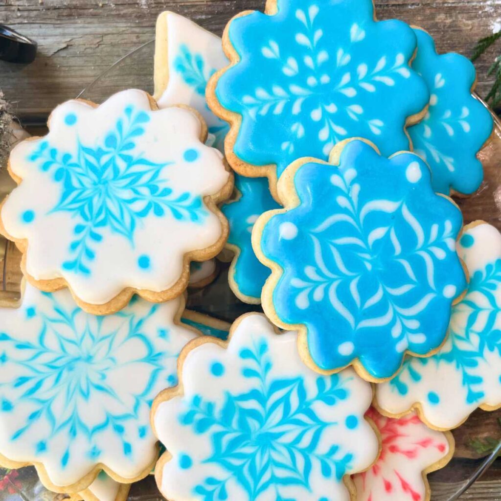 Cookies decorated as snowflakes on a glass plate.