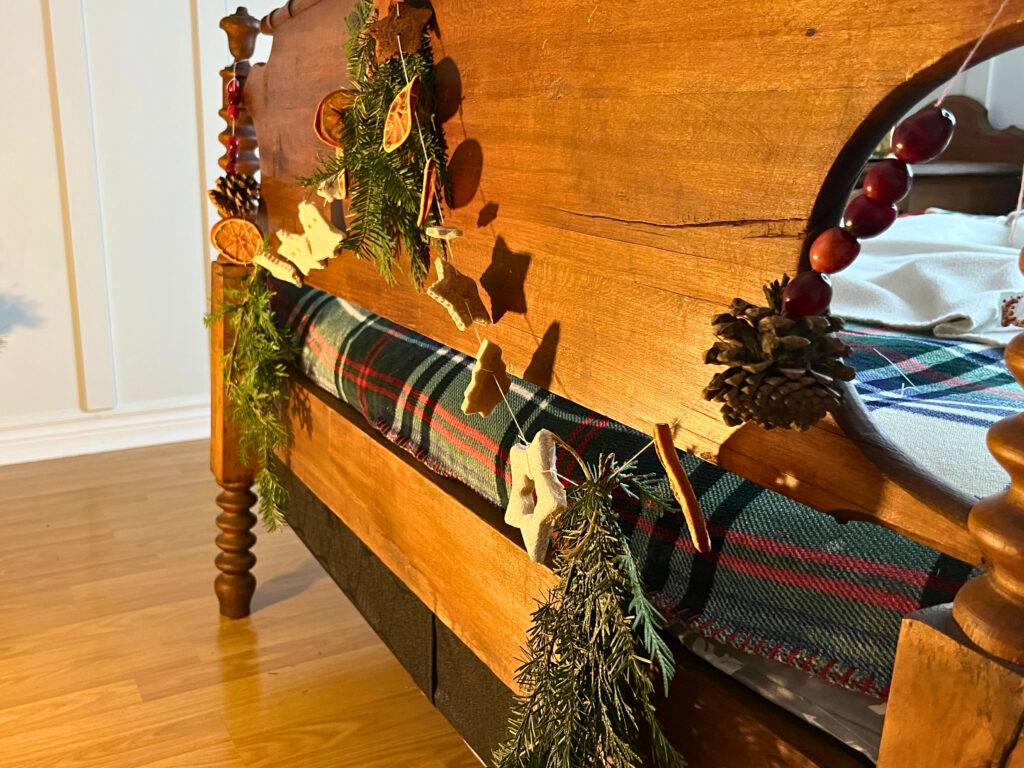 A natural Christmas garland attached to a bed footboard. It consists of salt dough, cinnamon dough, dried oranges, cranberries, and evergreen pieces.