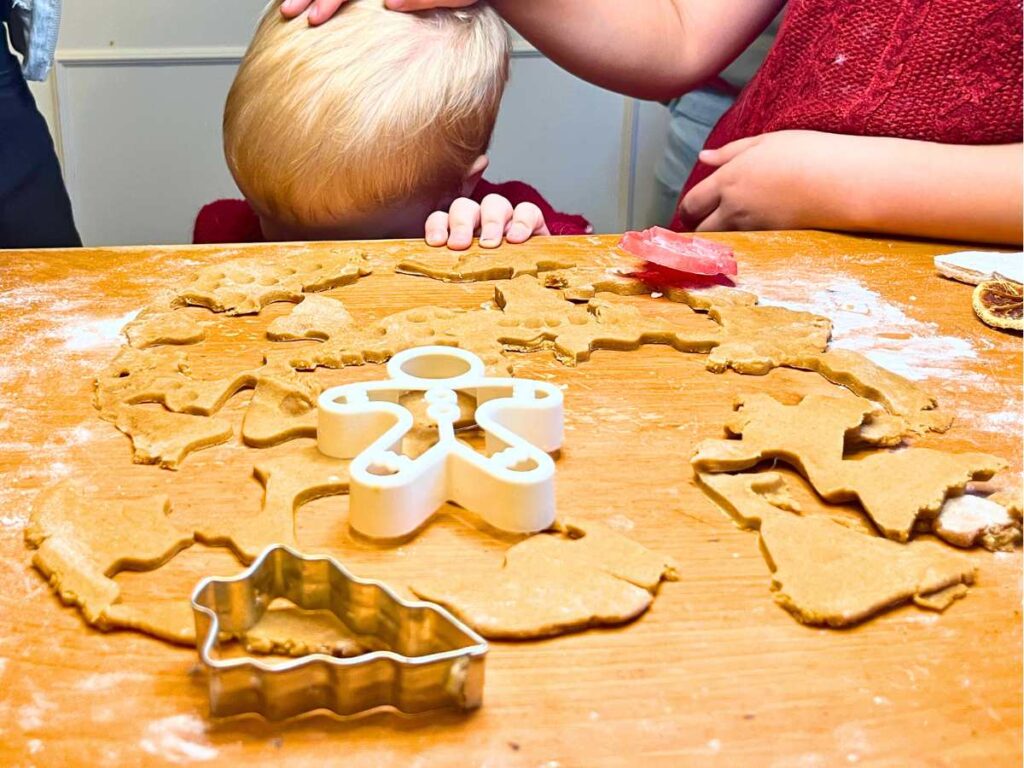 Gingerbread cookie dough rolled out on a wooden table and cut into shapes.