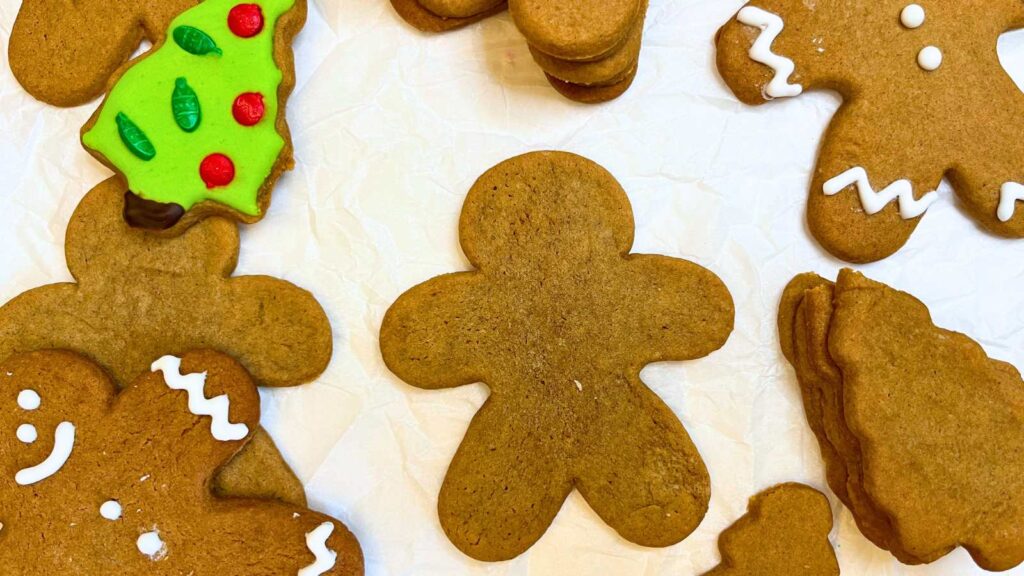 Some gingerbread cut out cookies on a piece of parchment paper. Some are decorated.