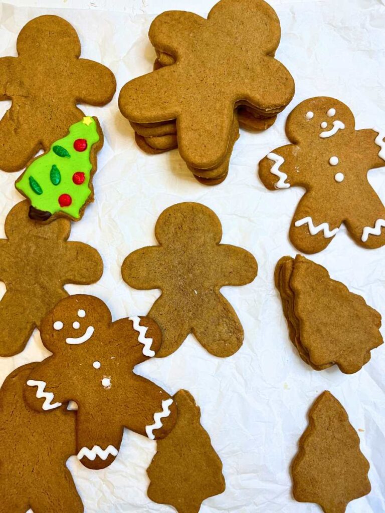 A collection of gingerbread men and cutouts on a piece of parchment paper. Some are decorated.