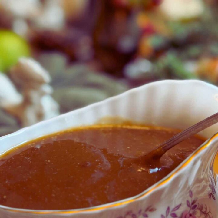 A gravy boat with gravy and a spoon inside.