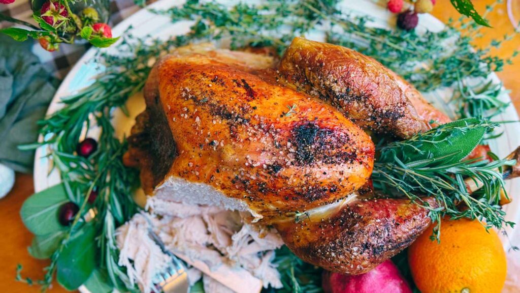 An overhead view of a roast turkey. It has some sliced. It is on a platter decorated with fresh herbs.