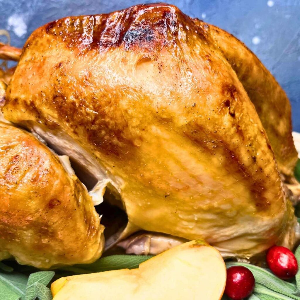 a side view of a roast turkey on top of sage leaves, apples, and cranberries.