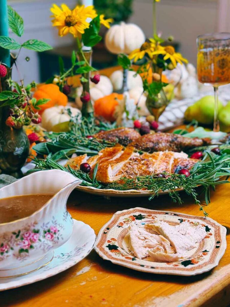 Sliced turkey on a platter with fresh herbs. There is a gravy boat in front.