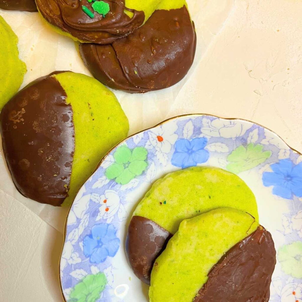 Two mint chocolate shortbread cookies on a blue and green floral plate. There are more on the table.