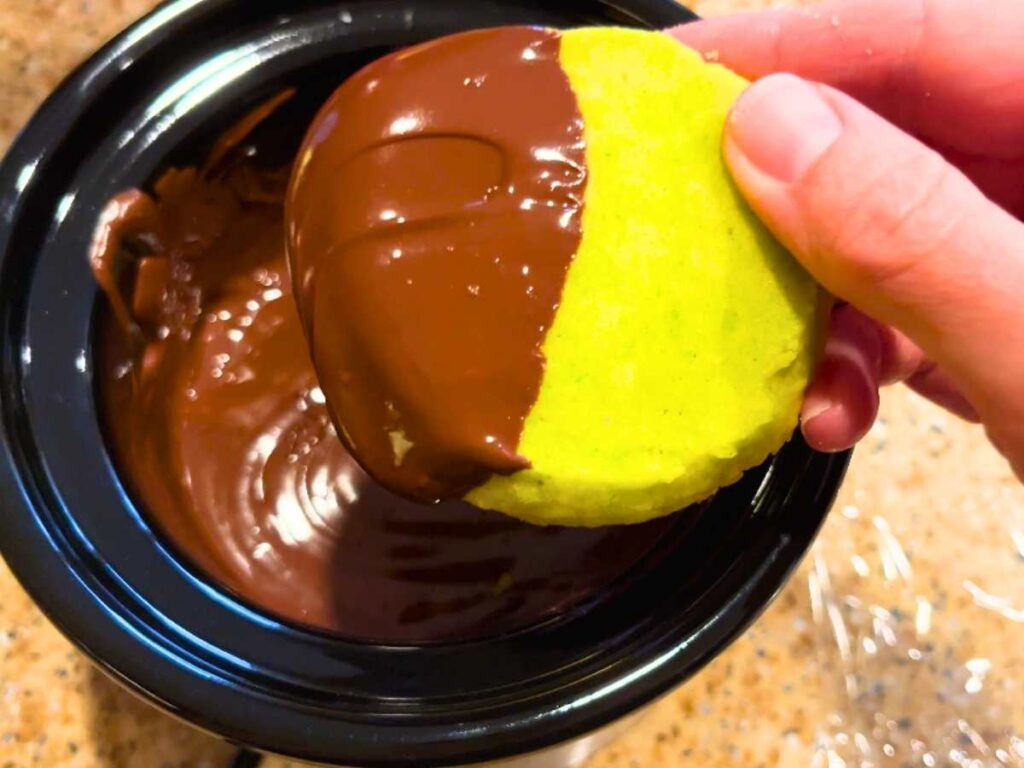 A woman is dipping mint shortbread cookies in melted chocolate.