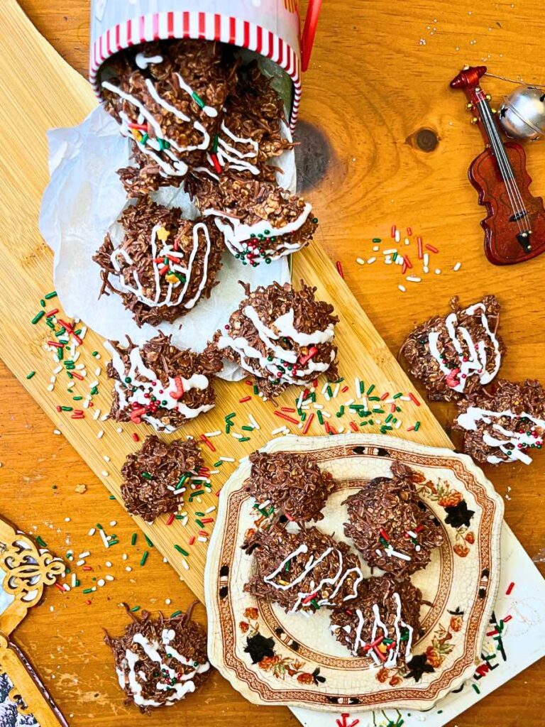 A wooden cutting board with decorated chocolate haystack cookies on top. There are some on a brown floral plate.