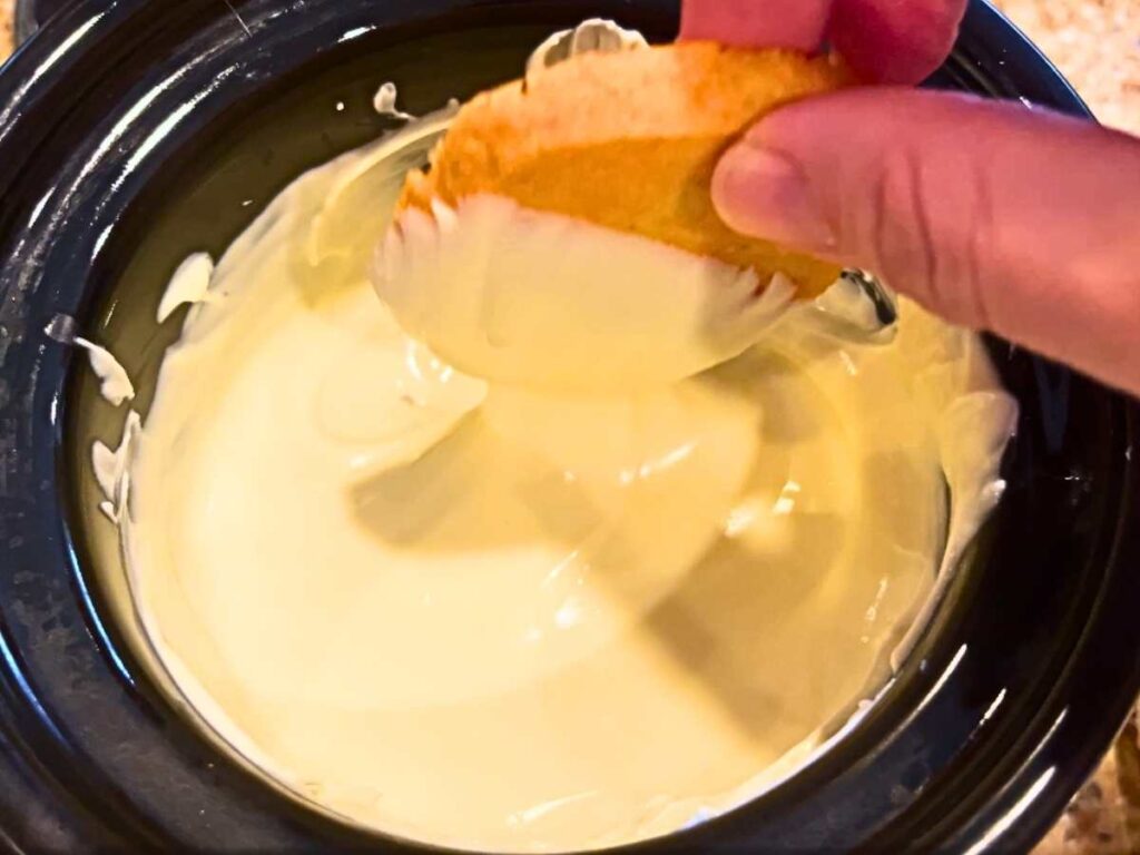 A woman dipping an orange cookie into melted white chocoalte.