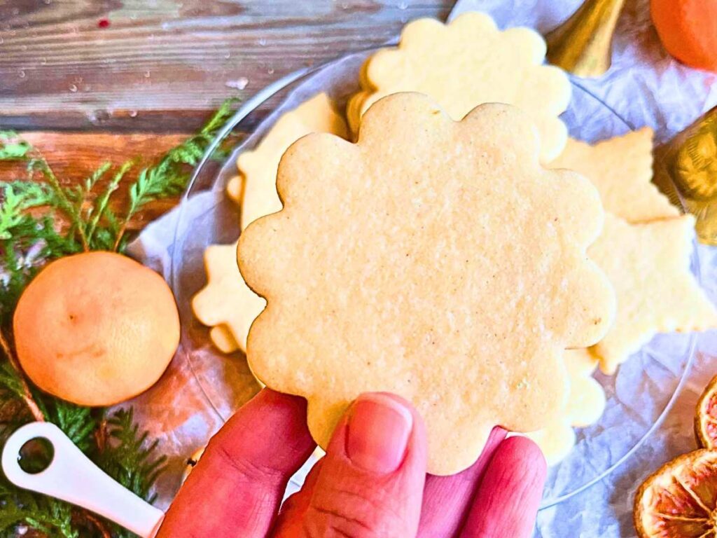 A woman is holding up a baked sugar cookie. there are more in the background.