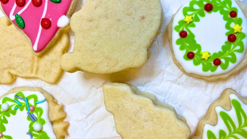 A collection of orange and cardamom sugar cookies on a piece of parchment paper. Some are decorated.