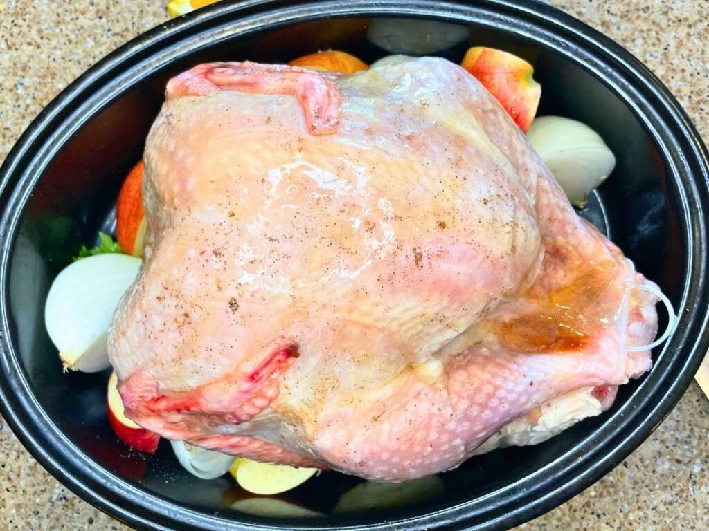 A raw turkey in a roasting pan surrounded by fruit and vegetables.