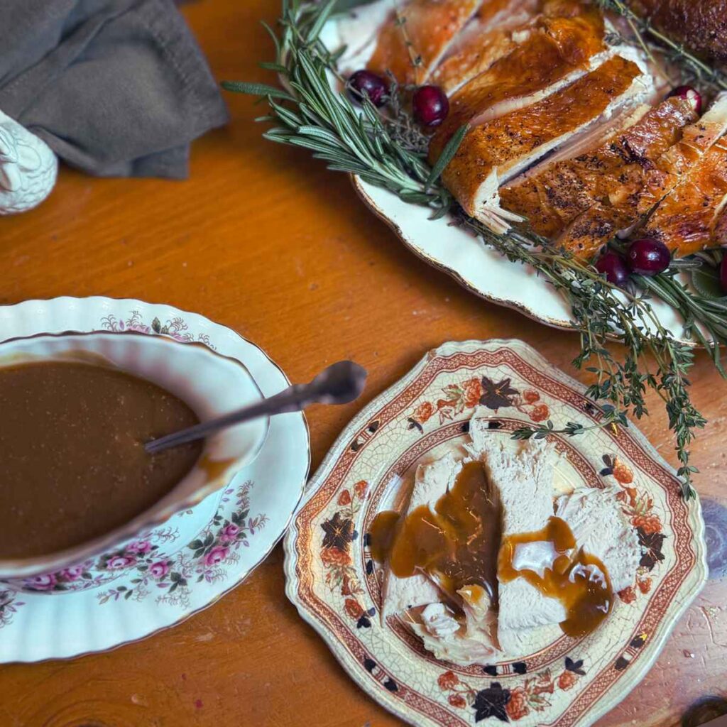 A table with gravy in a gravy boat and sliced turkey.