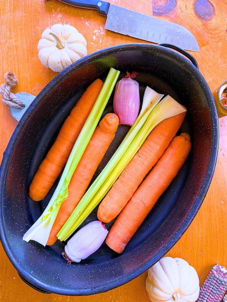A roasting pan with carrots, celery, and a shallot.