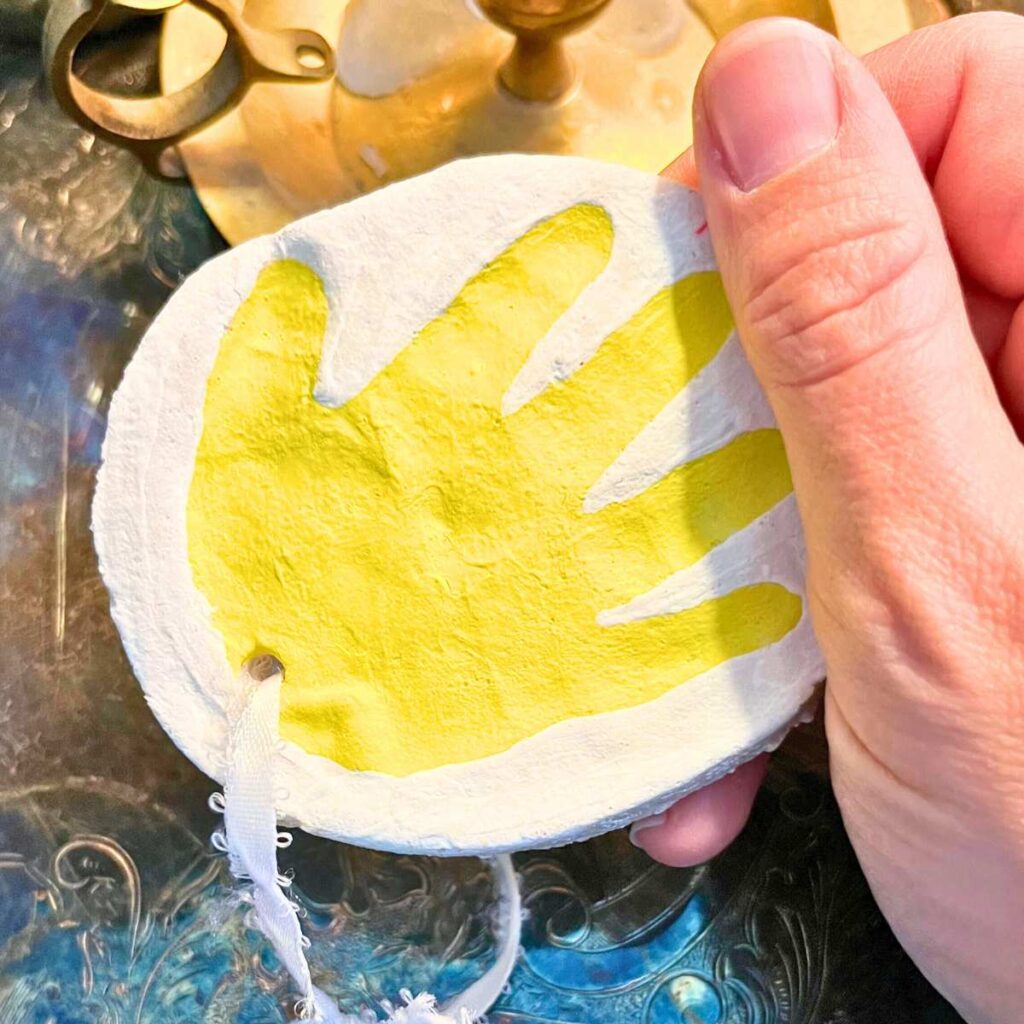 There is a woman holding a handprint ornament. It is painted yellow.