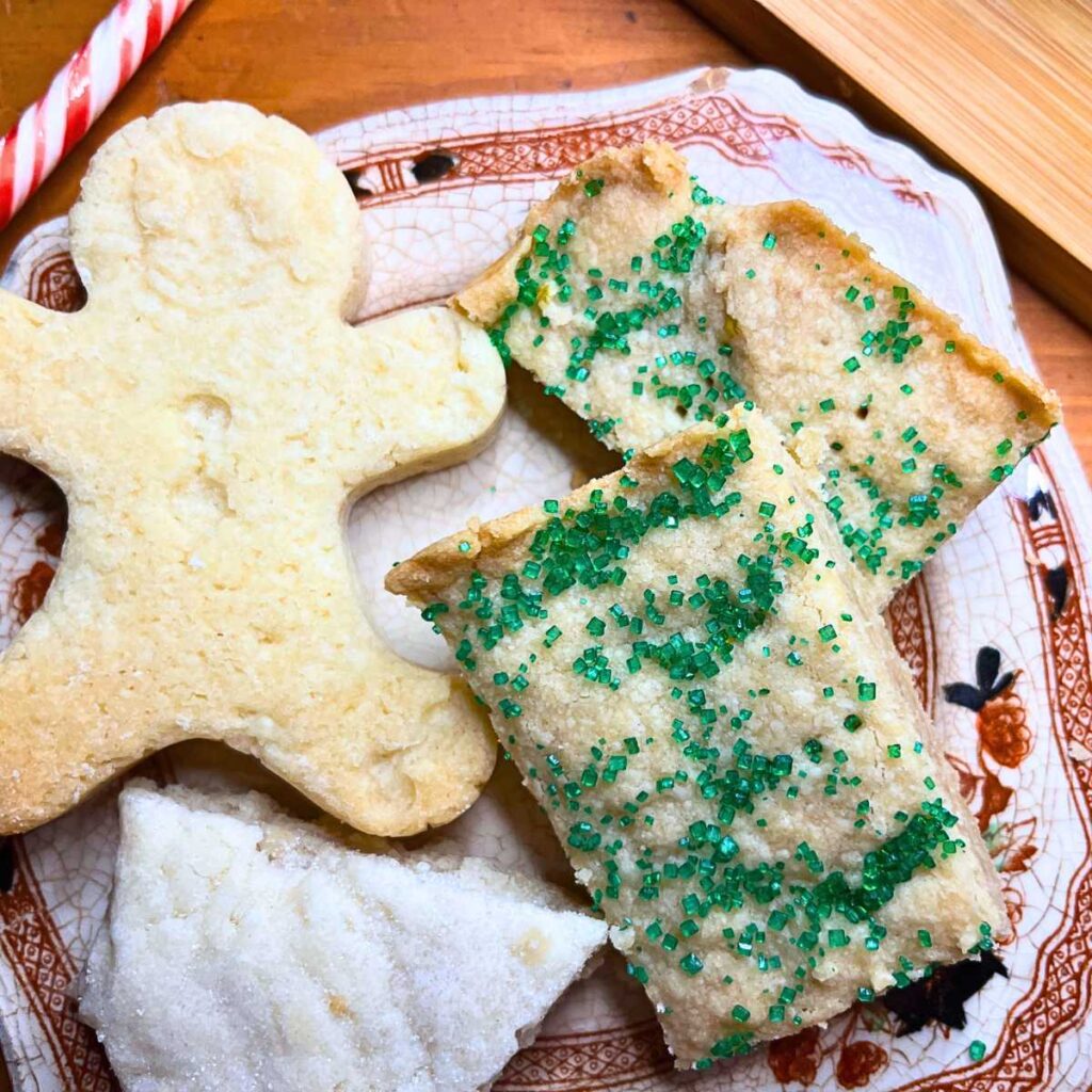 Some shortbread cookies on a brown floral plate. Some are dusted with green sanding sugar, some are in the shape of gingerbread men, some are wedge shape.