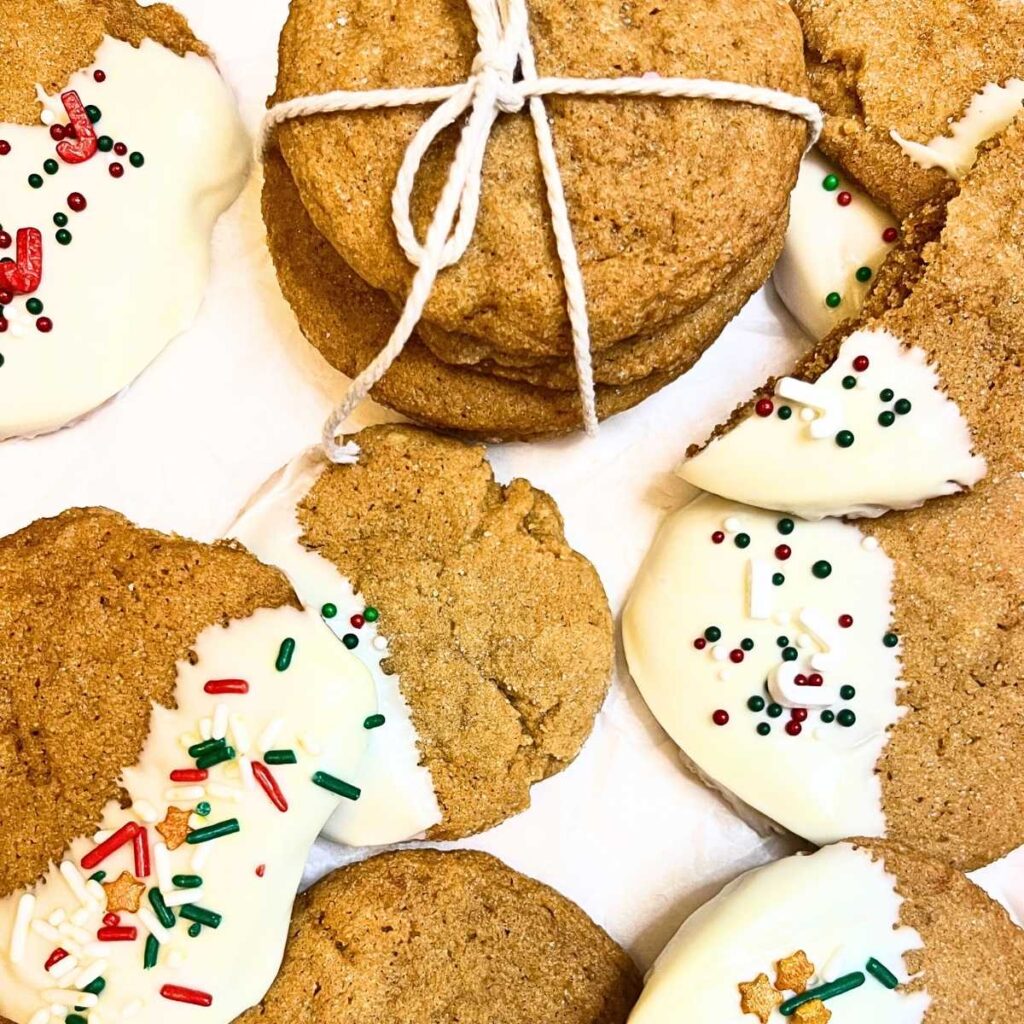 Gingerbread cookies stacked and tied with kitchen twine. There are more cookies decorated with white chocolate and spirnkles.