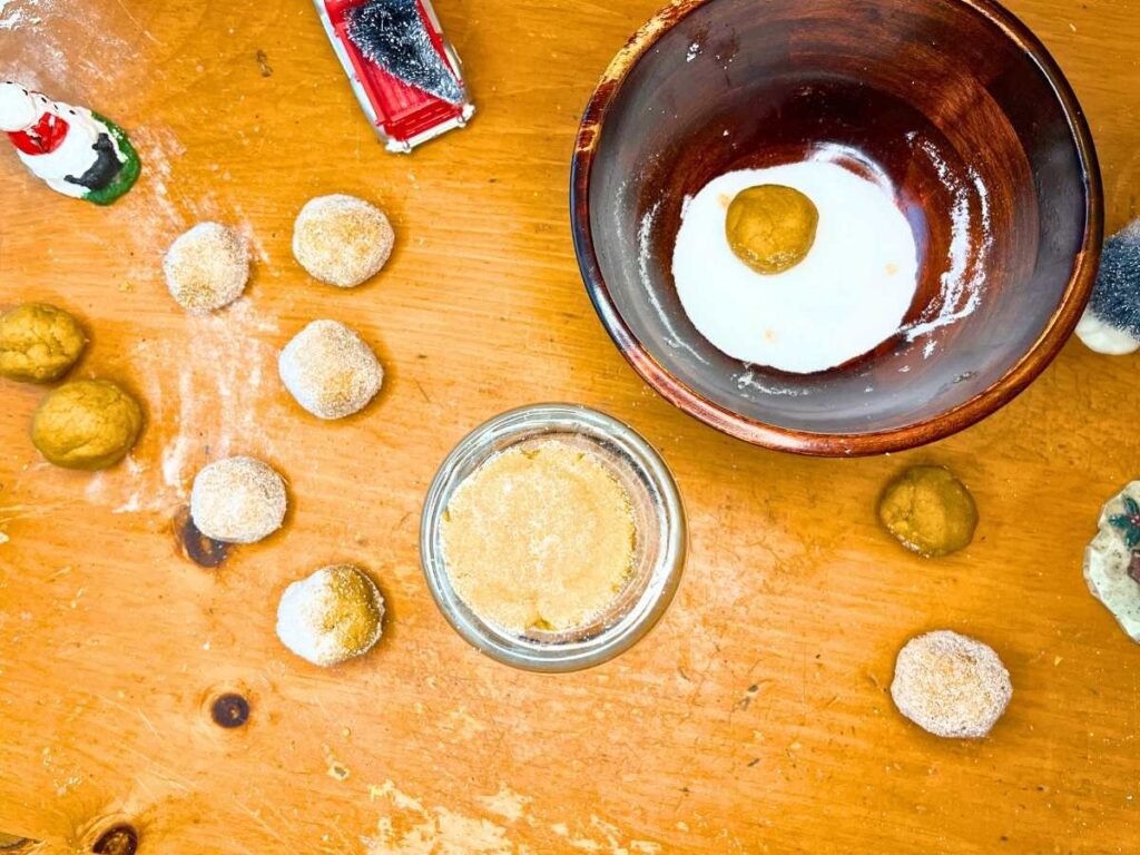 Rolled gingerbread cookie dough. There is one in a bowl of sugar and one flattened on top of a glass.