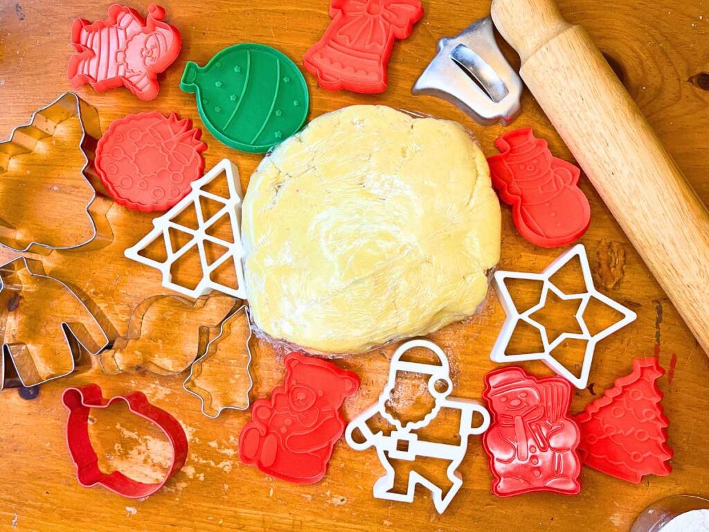 Some sugar cookie dough surrounded with cookie cutters and a rolling pin.