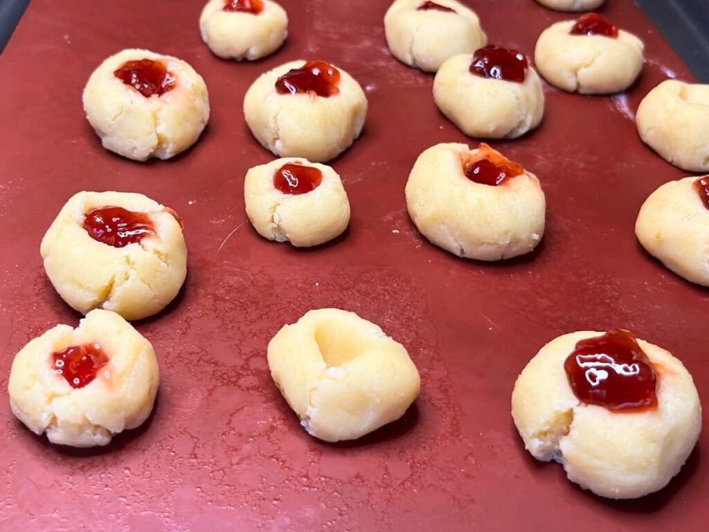 A collection of unbaked thumbprint cookies with jam in the centre.