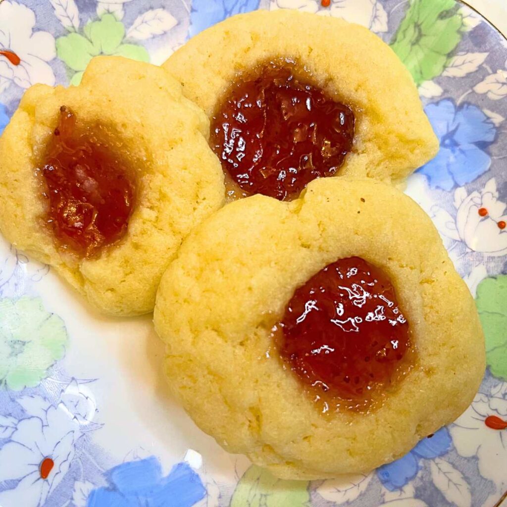 Three thumbprint cookies with jam centre on a blue floral plate.