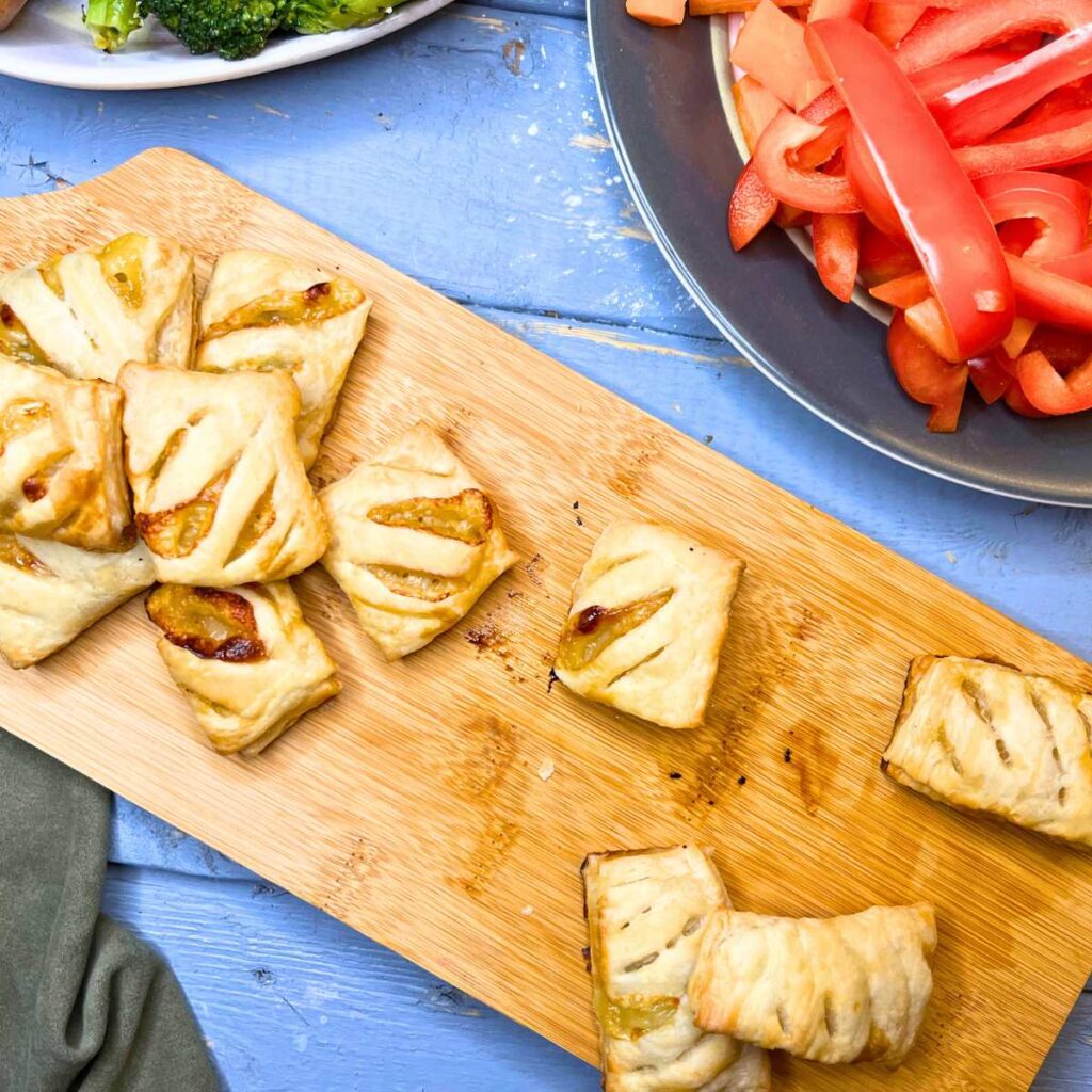 A wooden serving tray with puff pastry appetizers that are filled with Brie and honey.