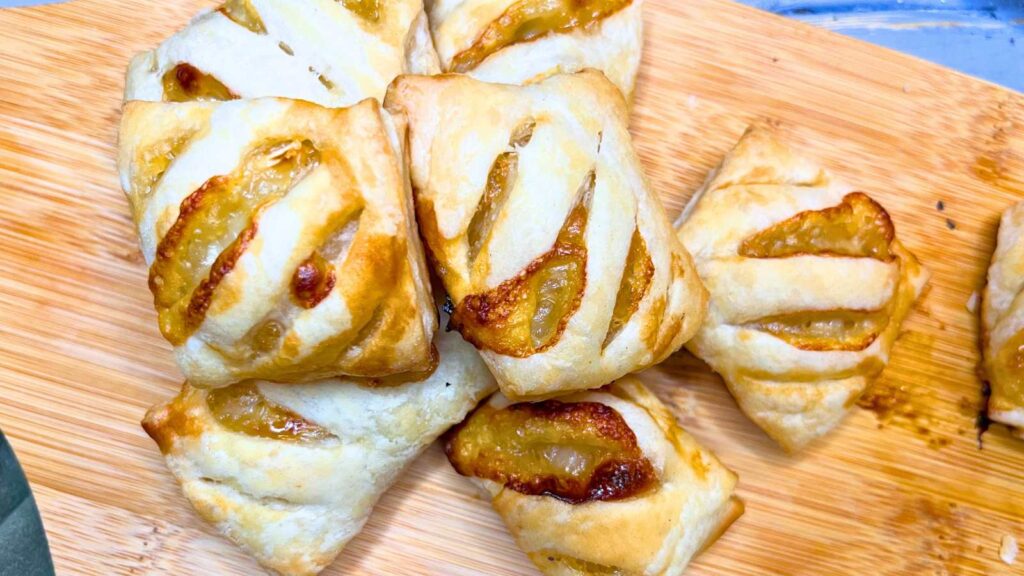 A wooden serving tray with puff pastry appetizers filled with Brie and honey.