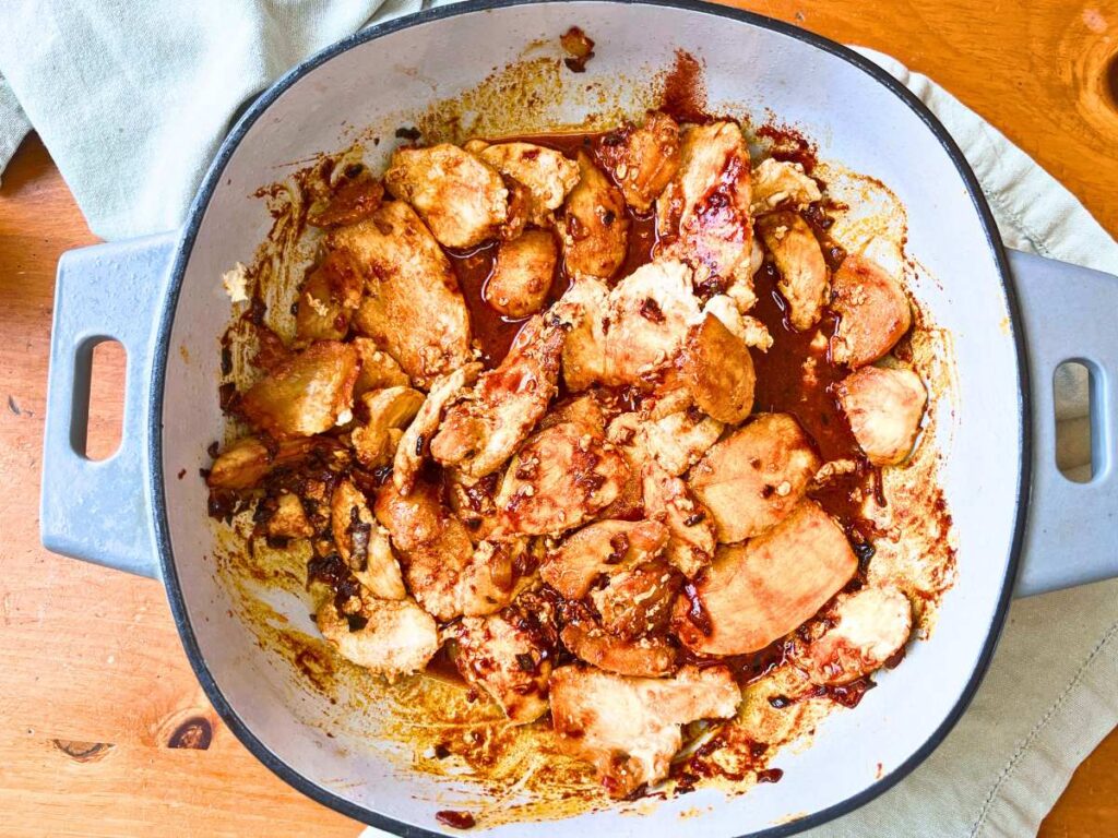 A Dutch oven with pieces of chicken, onions, and white wine inside.