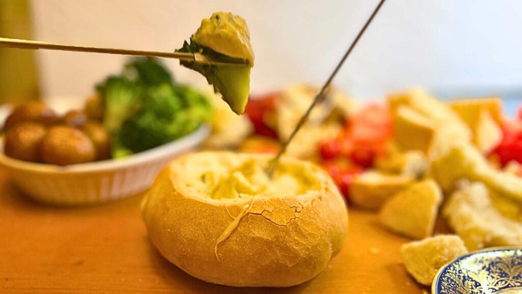 A cheese fondue in a bread bowl. A spear of broccoli is being dipped in cheese.