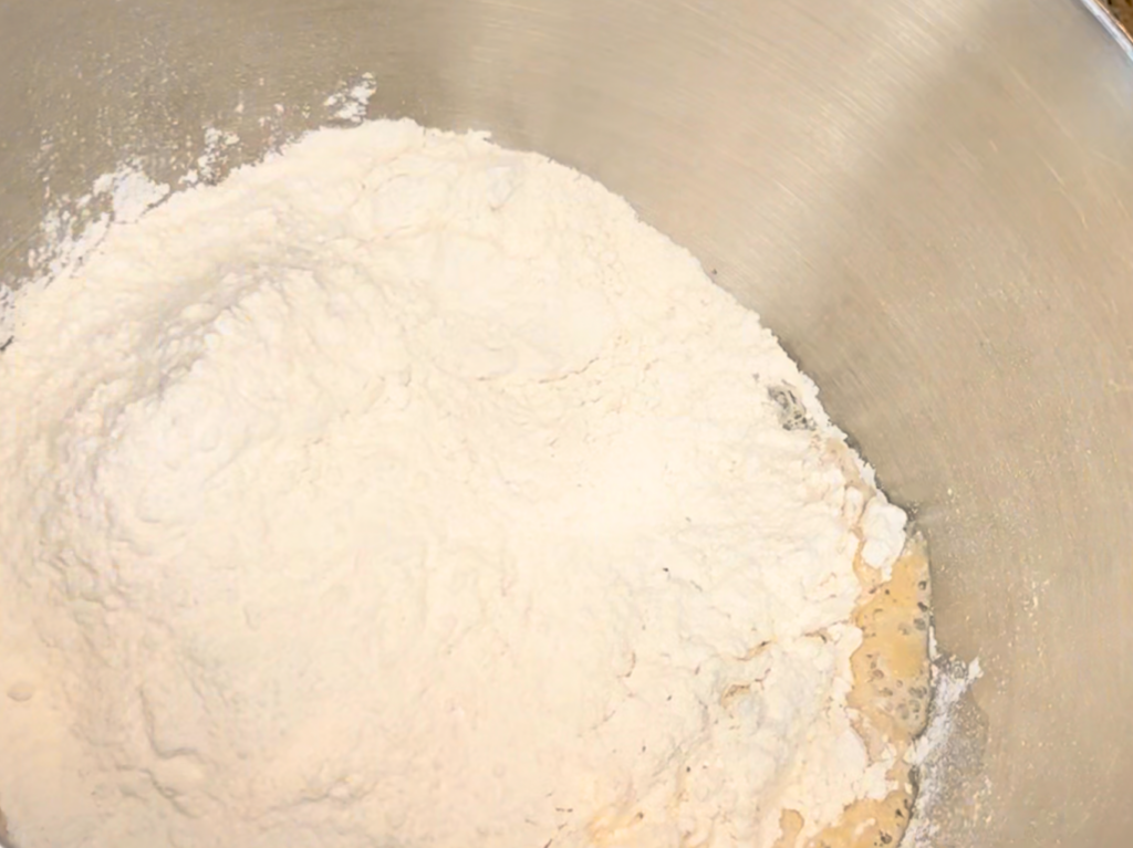 A bowl with milk, water, yeast, and salt. Flour has been added on top.
