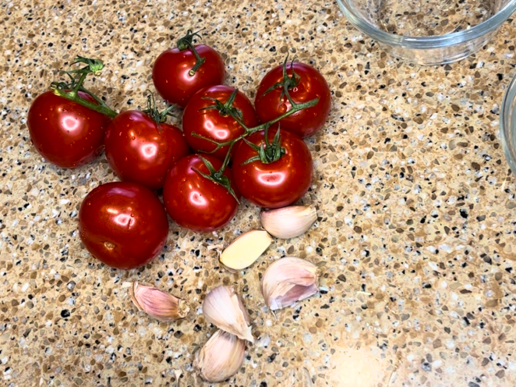 8 plum tomatoes and 6 cloves of garlic on a countertop.