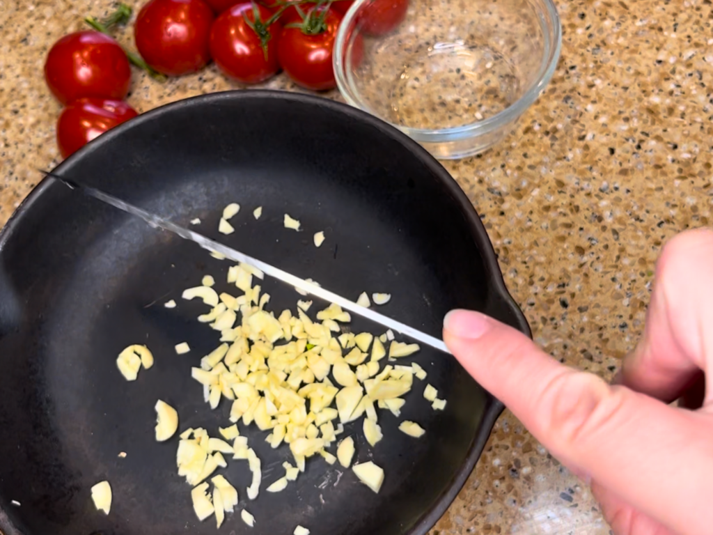 Woman adding minced garlic to a pan.