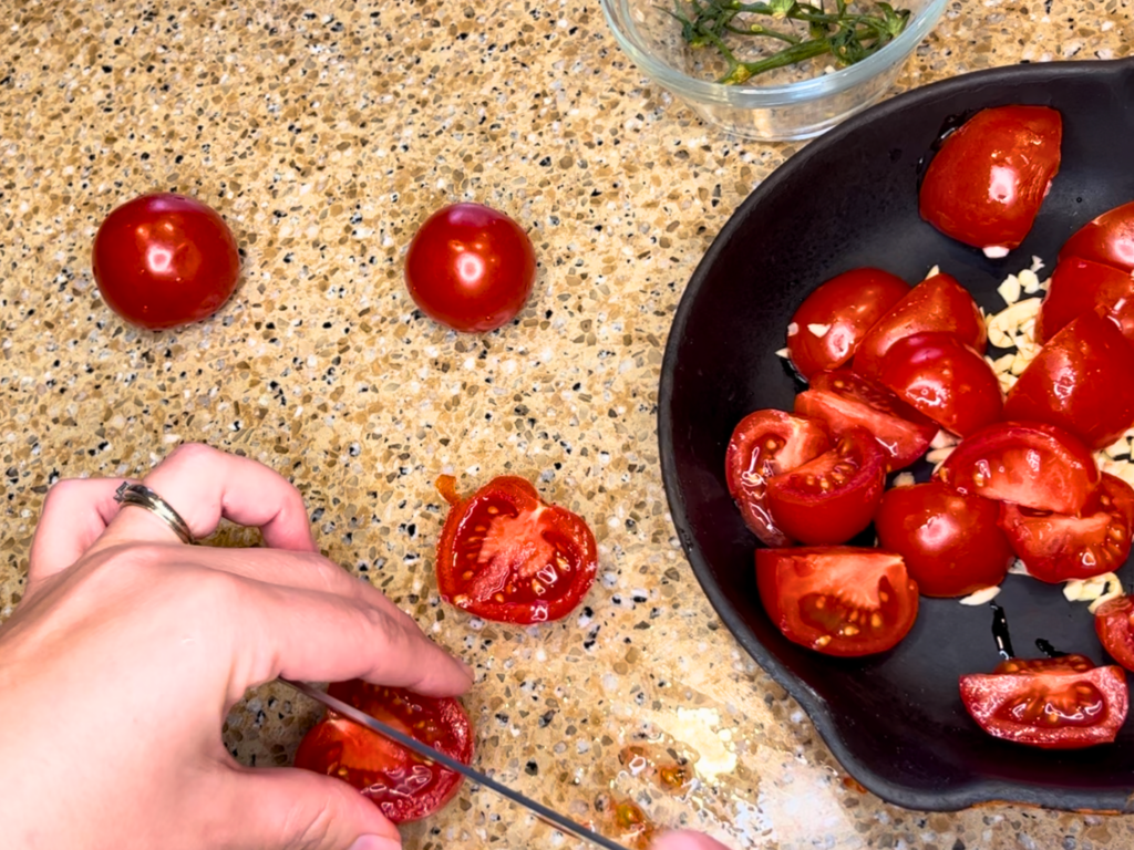 Woman cutting plum tomatoes and adding them to a pan with garlic.