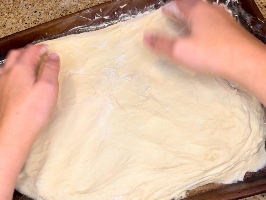 Woman spreading pastry dough out onto a baking sheet.