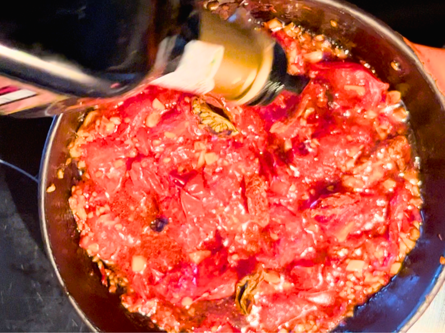 Woman adding balsamic vinegar to a pan of cooked tomatoes and garlic.