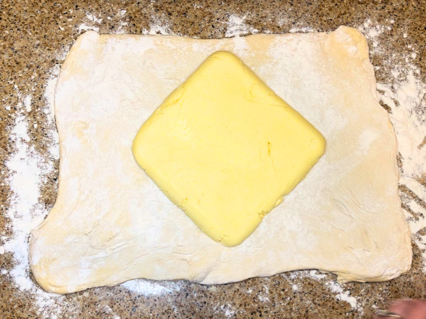 A square of butter placed diagonally onto pastry dough.