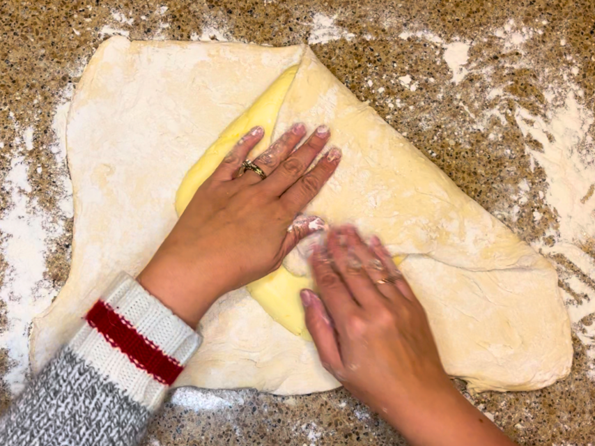 Woman folding the corners of the pastry dough in to seal in the butter.