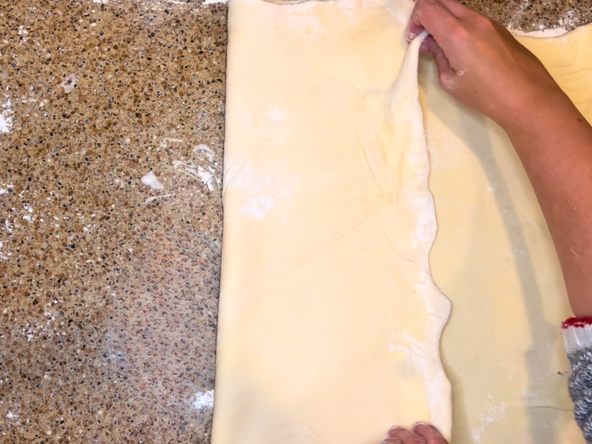 Woman folding puff pastry dough into thirds.