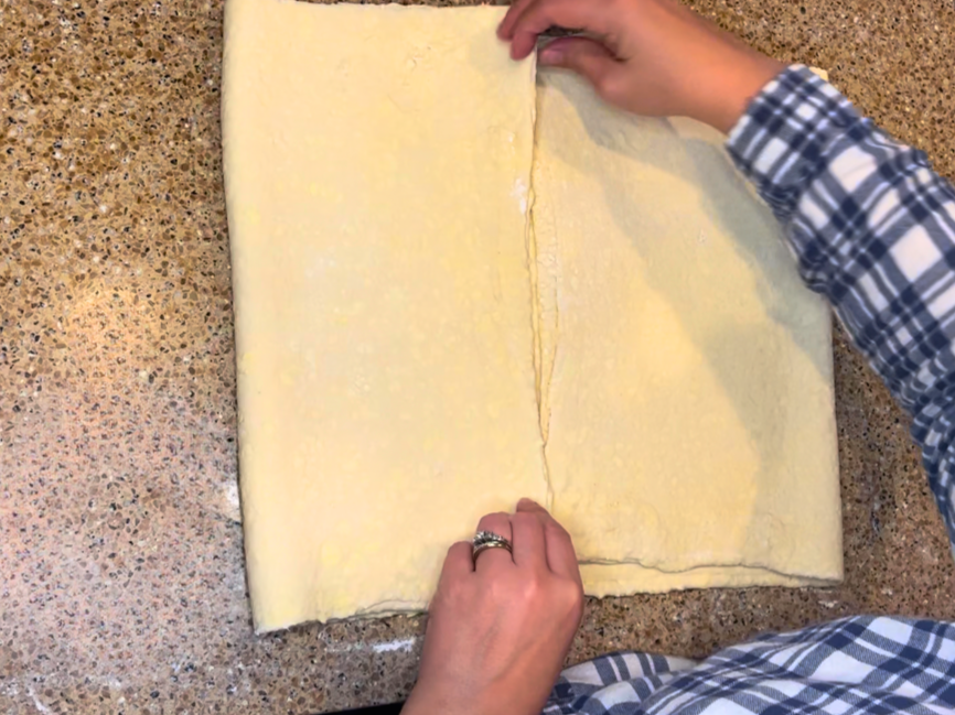 A woman folding puff pastry dough into quarters.
