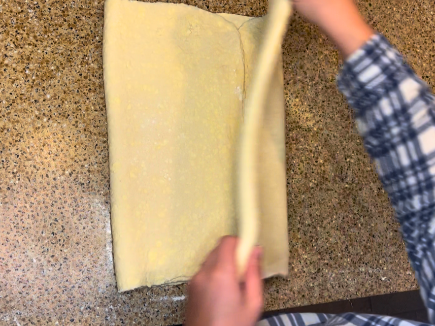 Woman folding puff pastry dough into quarters.