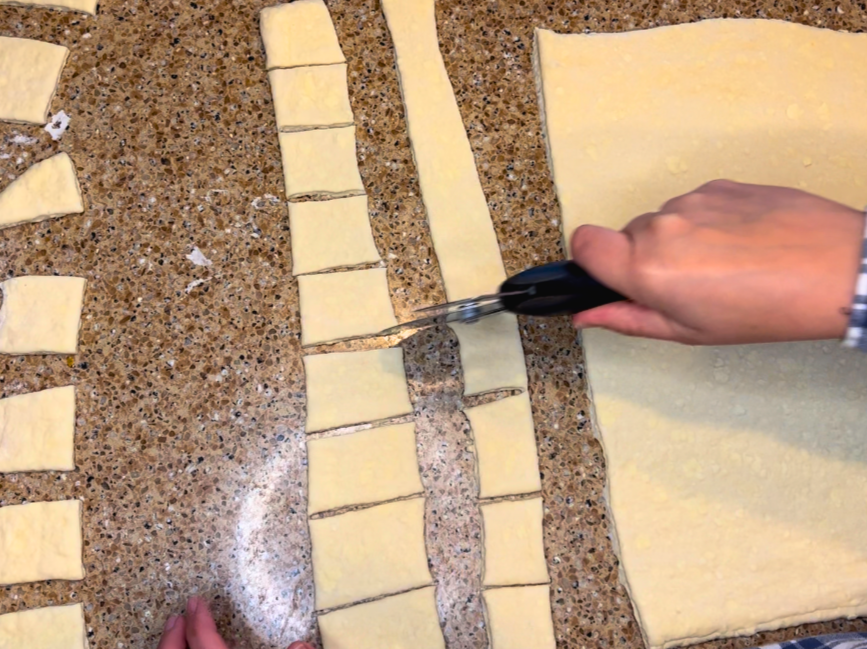 Woman cutting puff pastry dough into squares with a pizza cutter.